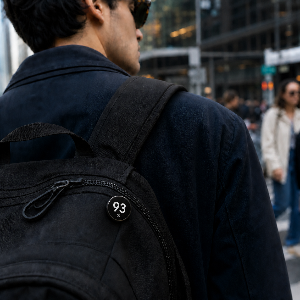 Close-up of a commuter wearing the black PERCENT badge showing 93 percent on a backpack in the city